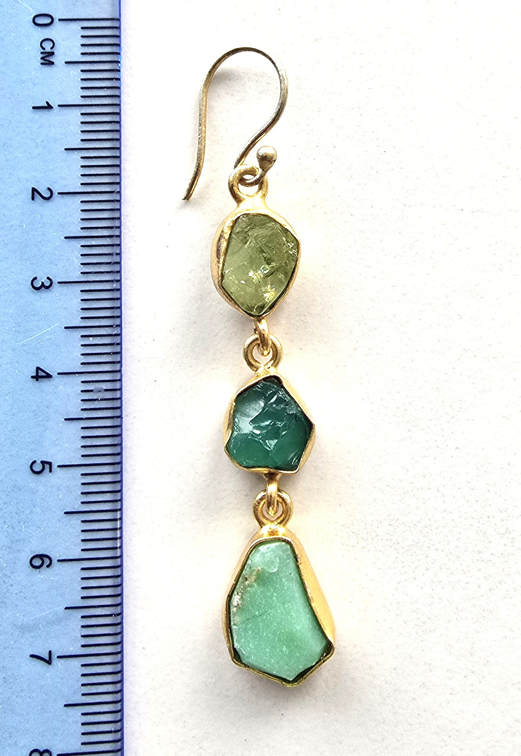 Gold earrings with green stones next to a ruler on a white background